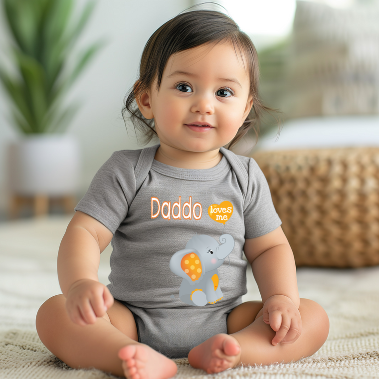 A smiling baby girl wearing a grey onesie with an elephant design sits on the floor.