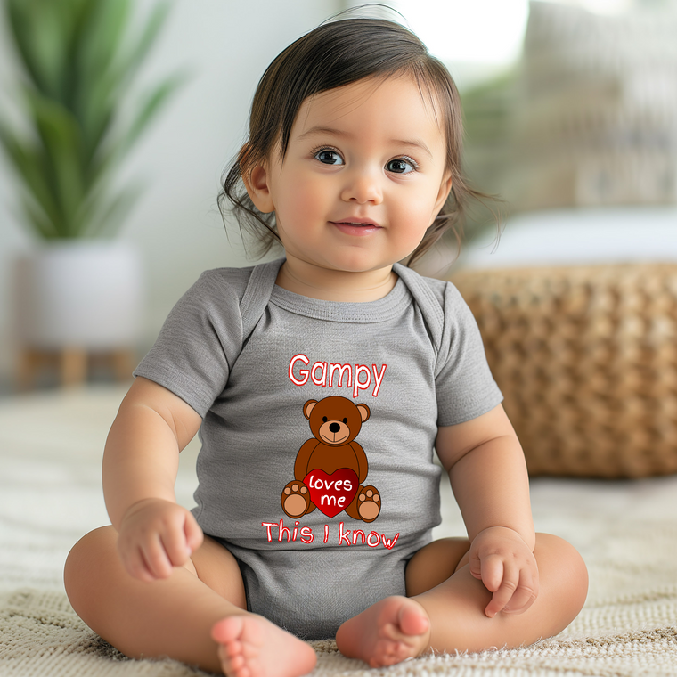 A smiling baby girl wearing a gray onesie with a teddy bear graphic and text.