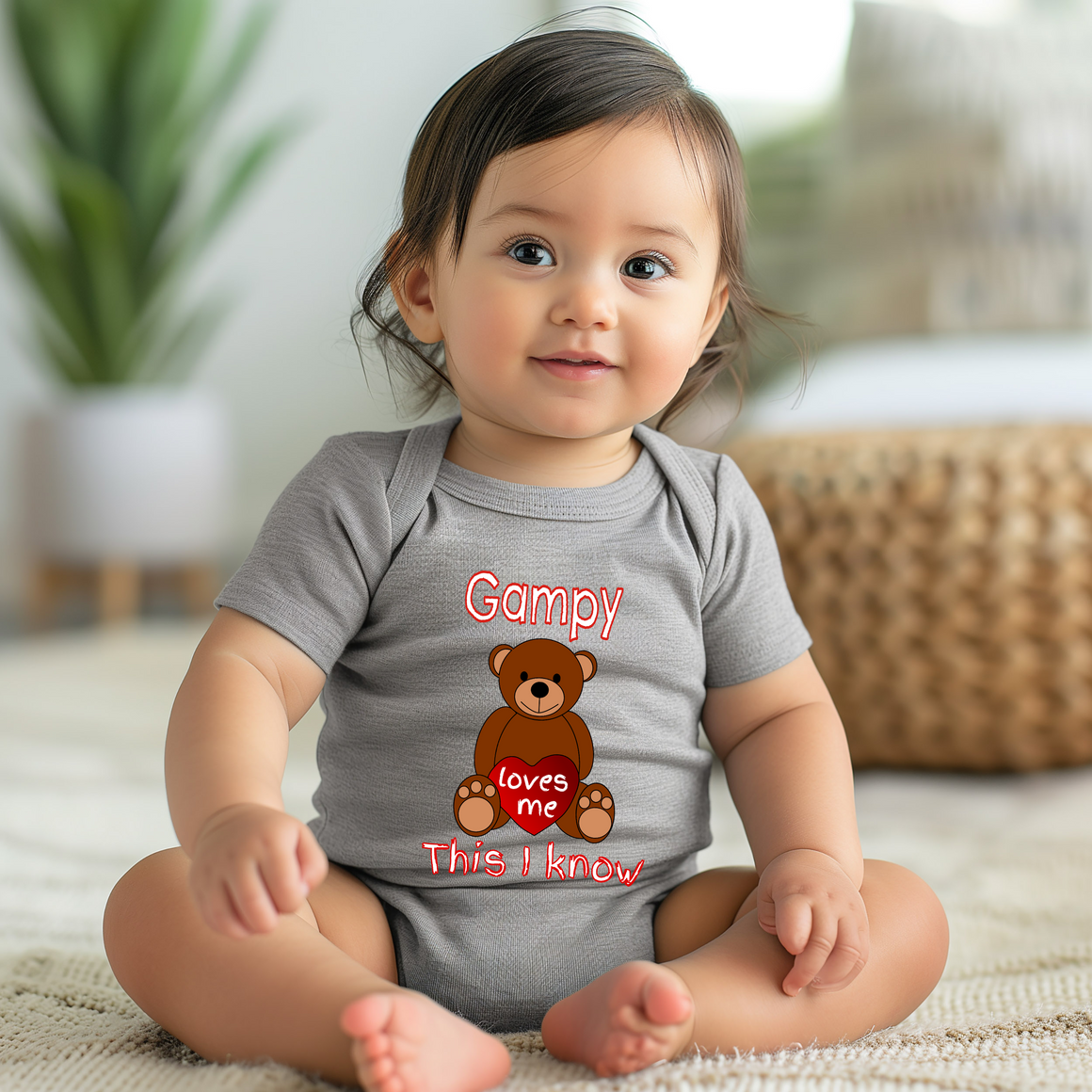 A smiling baby girl wearing a gray onesie with a teddy bear graphic and text.