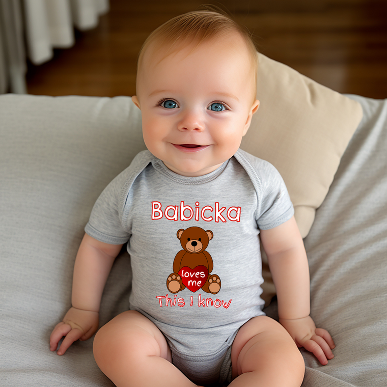 A smiling baby wearing a gray onesie with a teddy bear and the text "Babika" and "This I know" printed on it.