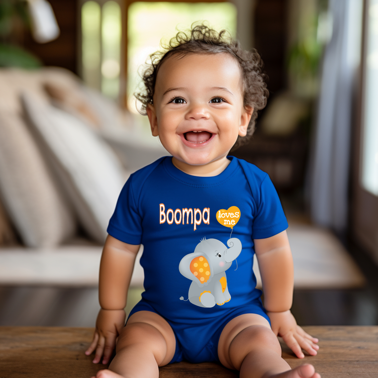 A smiling baby boy wearing a blue onesie with an elephant design sits on a wooden surface.