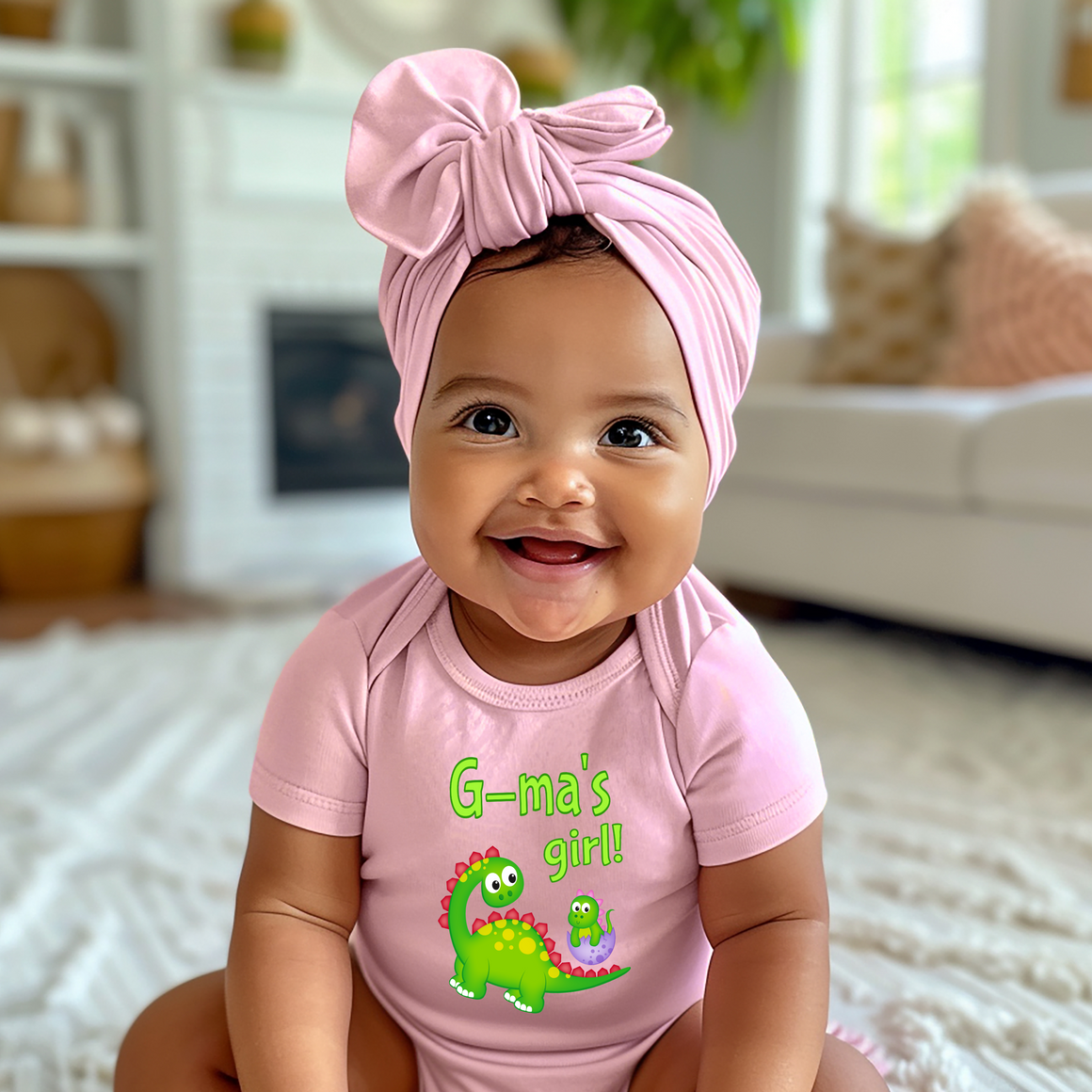 A smiling baby girl wearing a pink headband and a pink onesie with a dinosaur graphic, sitting on a white rug in a living room.