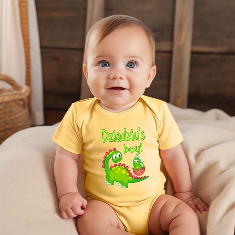 A smiling baby wearing a yellow onesie with a dinosaur design and the text "Dzaidzi's boy!"
