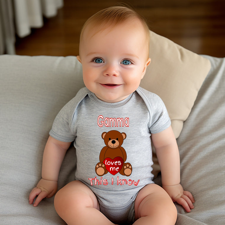 A smiling baby wearing a gray onesie with a teddy bear graphic and the text "Gamma loves me This I know" printed on it.