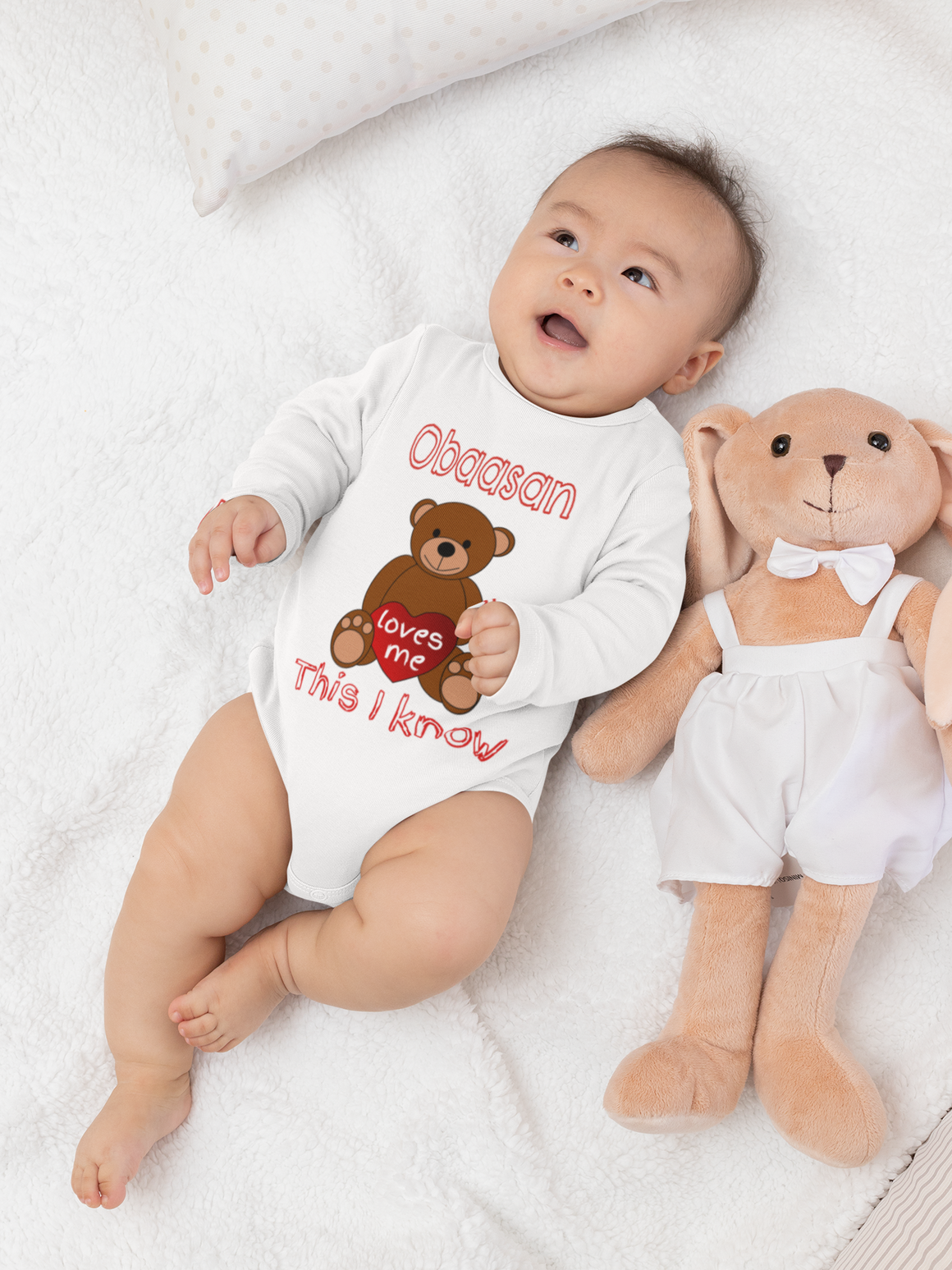 A baby lying on a white blanket next to a stuffed teddy bear.