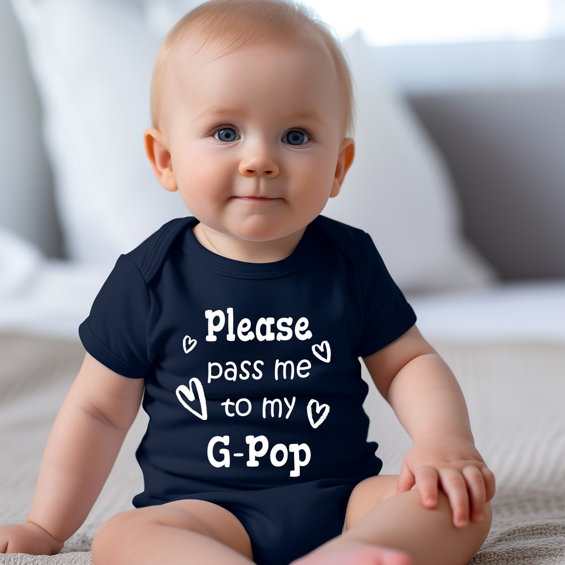 A smiling baby wearing a navy blue onesie with the text "Please pass me to my G-pop" printed on it.