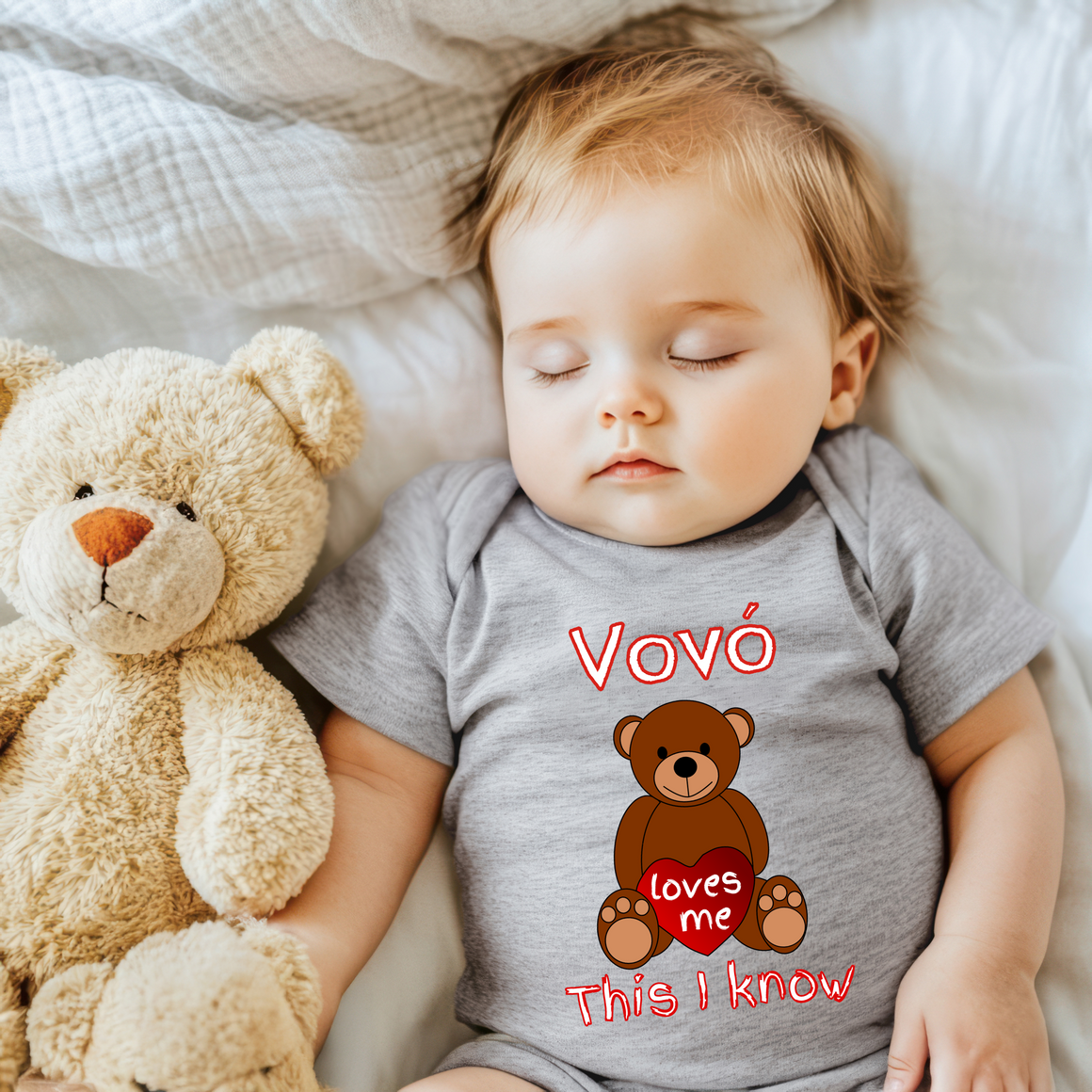 A sleeping baby wearing a gray onesie with a teddy bear and the text "VvoÁE loves me This I know" printed on it.