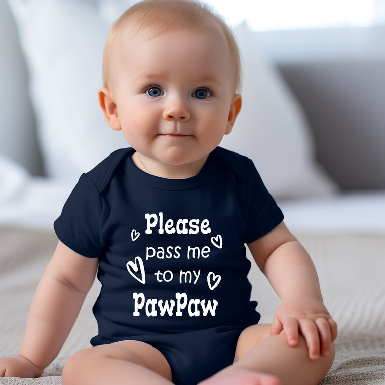 A smiling baby wearing a navy blue onesie with the text "Please pass me to my Paw Paw" printed on it.