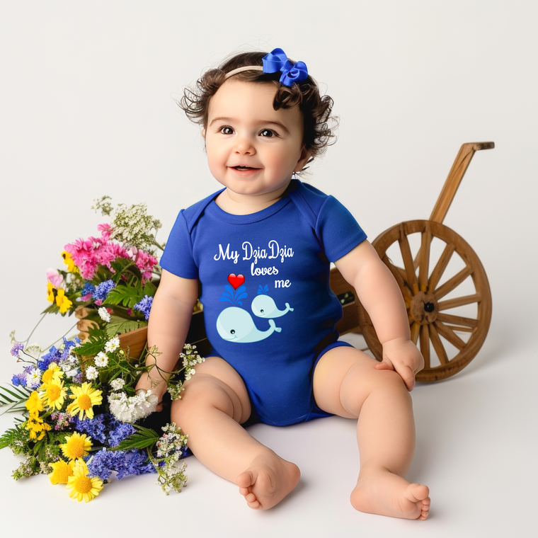 A smiling baby girl wearing a blue onesie with a whale design sits next to a wooden wagon filled with colorful flowers.