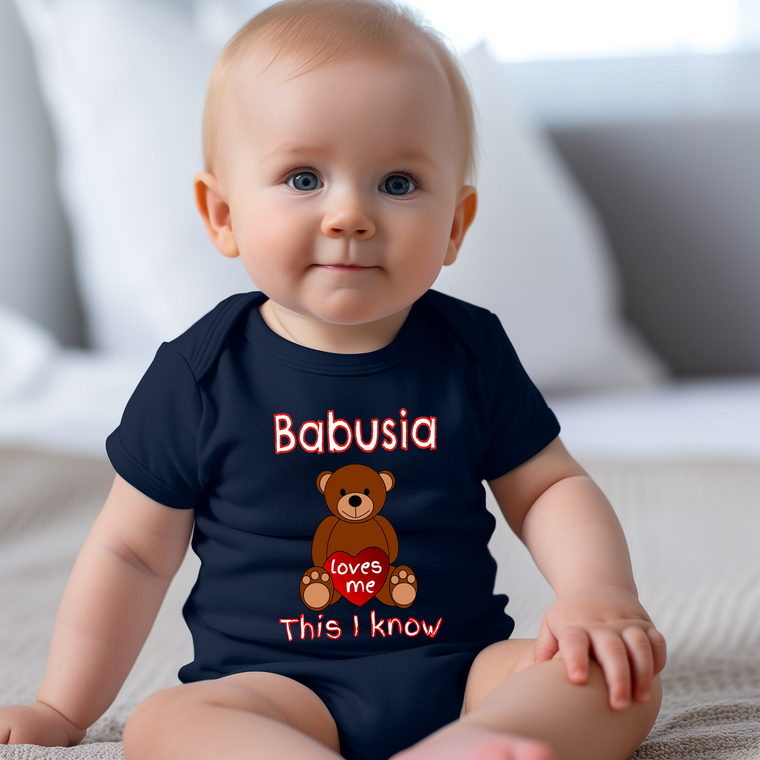 A smiling baby wearing a navy blue t-shirt with a teddy bear graphic and text that says "Babusia loves me This I know".