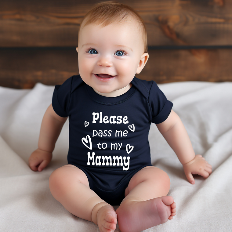 A smiling baby wearing a black onesie with the text "Please pass me to my Mammy" printed on it.