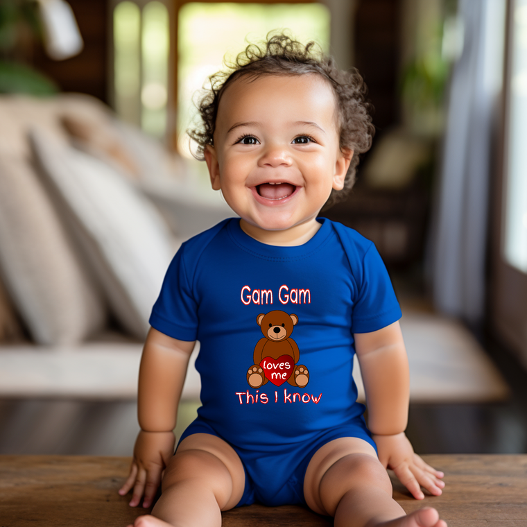 A smiling baby boy wearing a blue onesie with a teddy bear graphic and text on it.