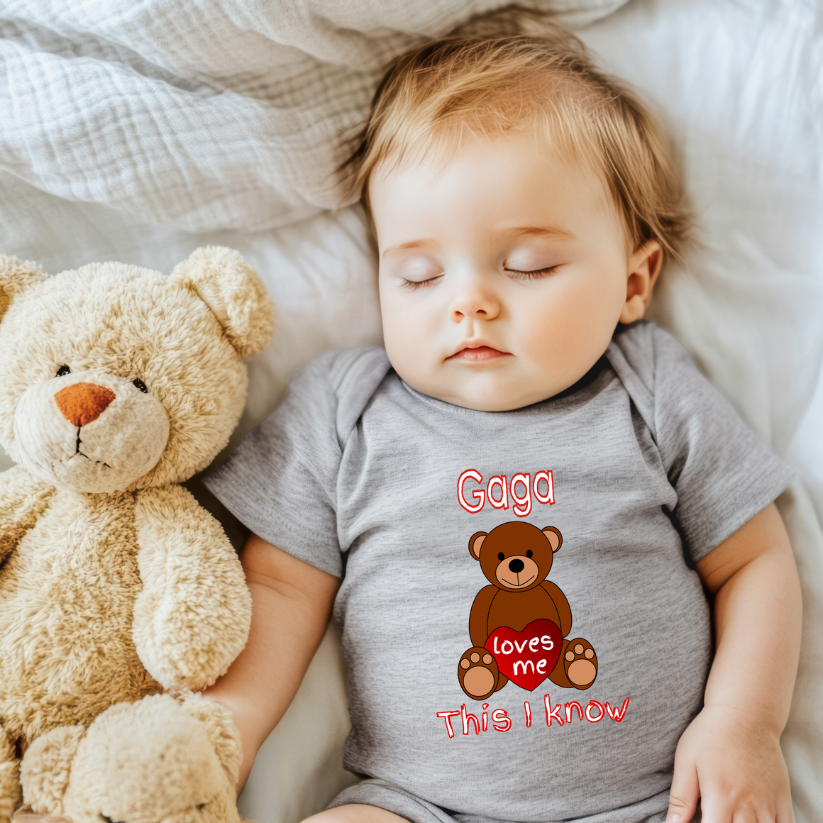 A sleeping baby wearing a grey onesie with a teddy bear and the text "Gaga loves me This I know" is pictured.