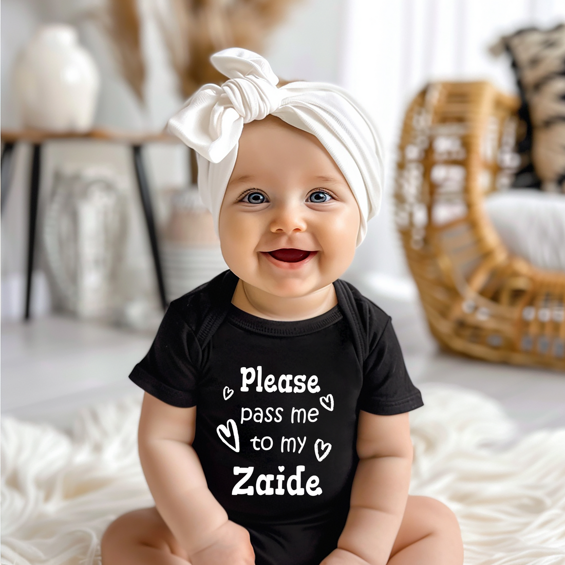 A smiling baby girl wearing a black t-shirt with a white bow on her head and a white headband.