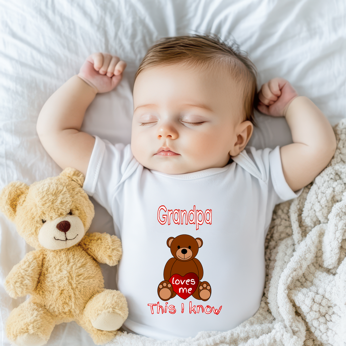 A sleeping baby wearing a white onesie with a teddy bear next to them.