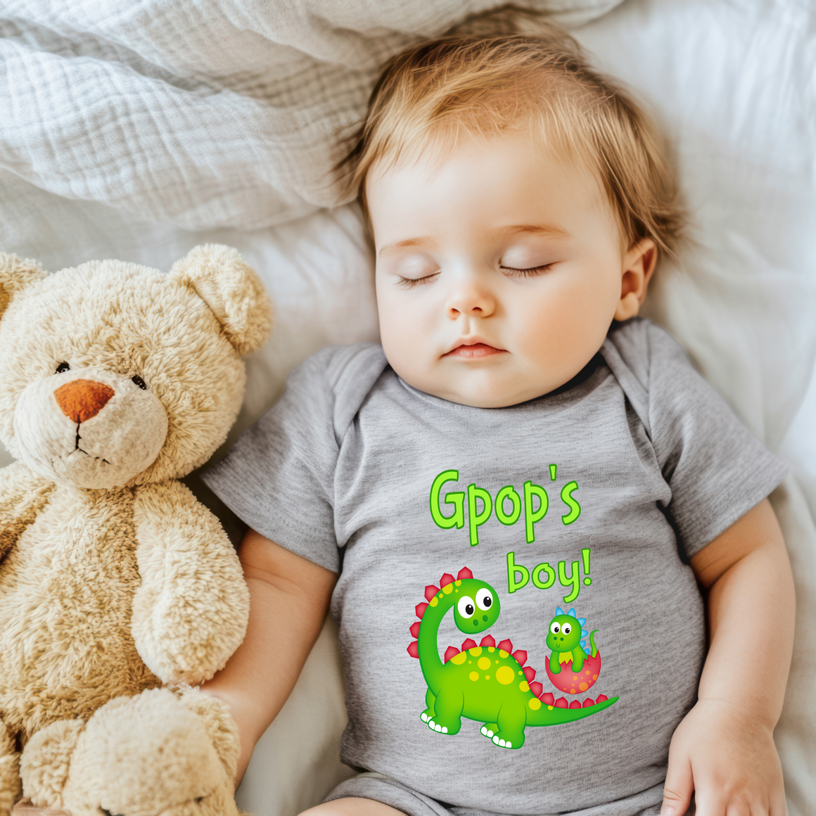A baby sleeping next to a teddy bear, with a t-shirt that says "Gpop's boy!"