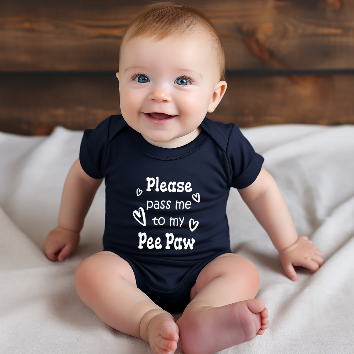 A smiling baby wearing a navy blue onesie with the text "Please pass me to my Pee Paw" printed on it.