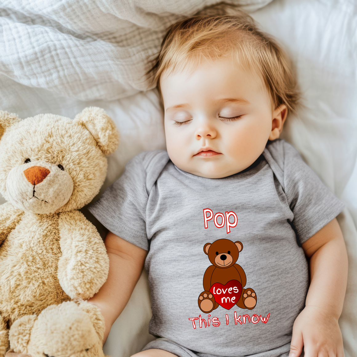 A sleeping baby wearing a gray onesie with a teddy bear next to them.