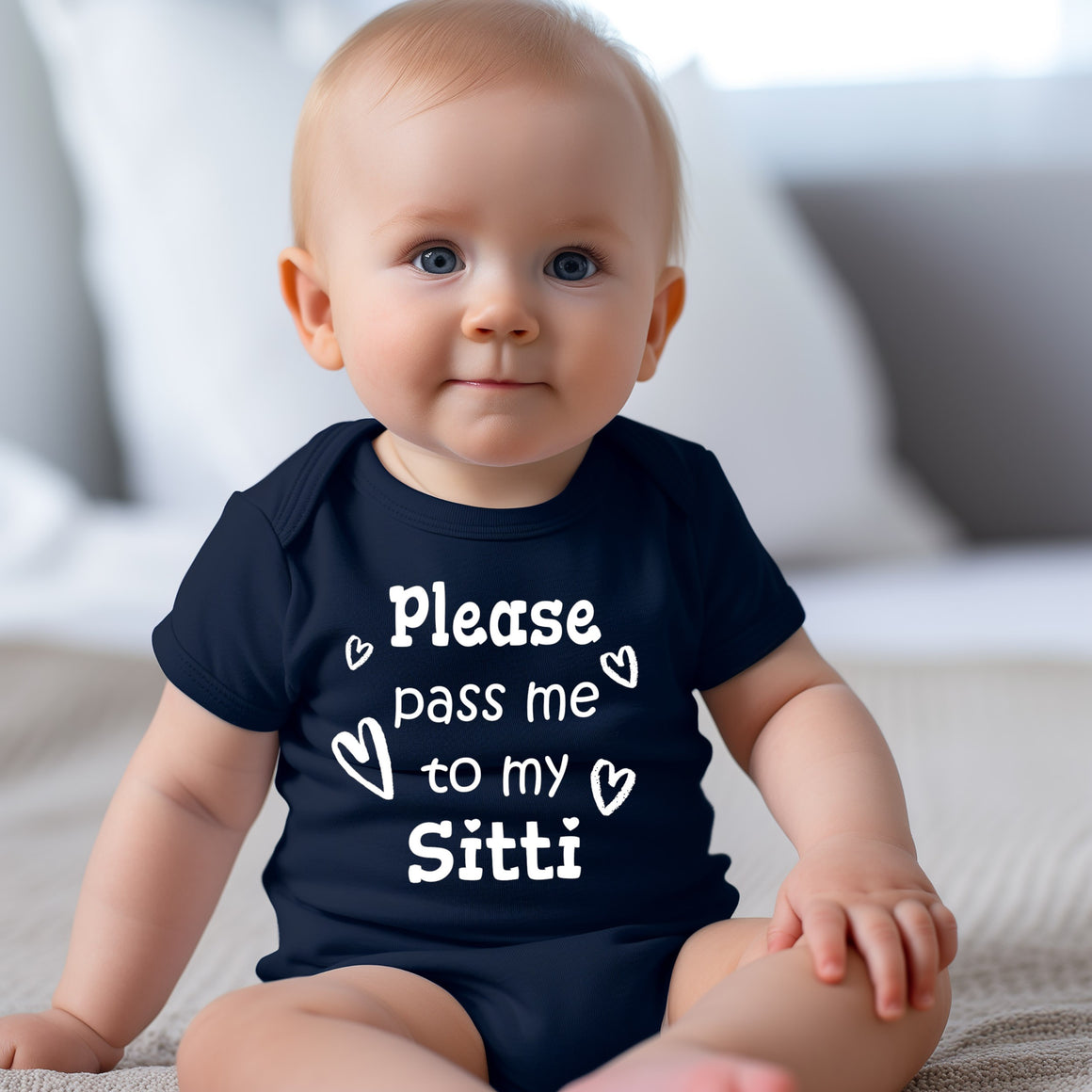 A smiling baby wearing a navy blue onesie with the text "Please pass me to my Sitti" printed on it.