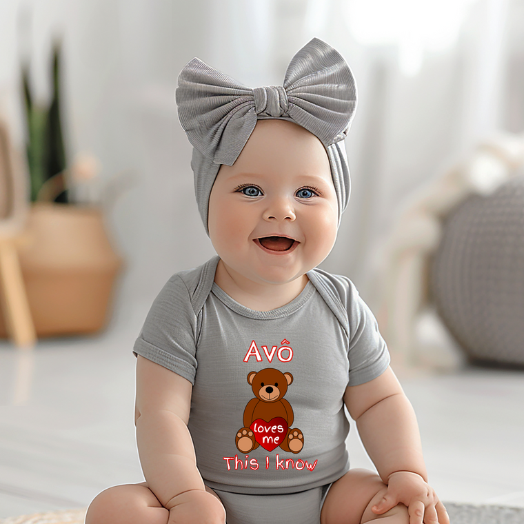 A smiling baby girl wearing a gray headband and a gray onesie with a teddy bear graphic and text.