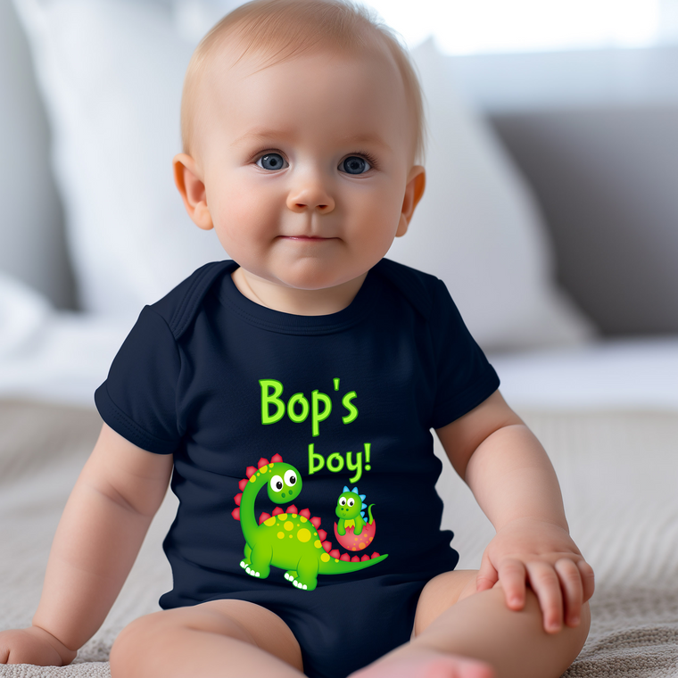 A smiling baby wearing a black t-shirt with a dinosaur graphic and text that says "Bop's boy!".