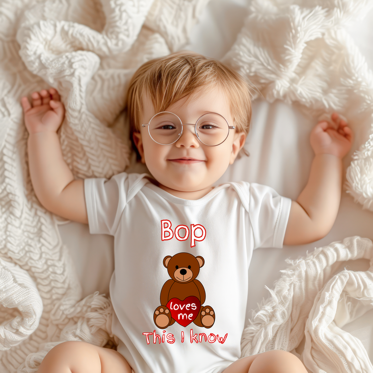 A smiling baby wearing a white onesie with a teddy bear graphic and the text "Bop loves me" printed on it.
