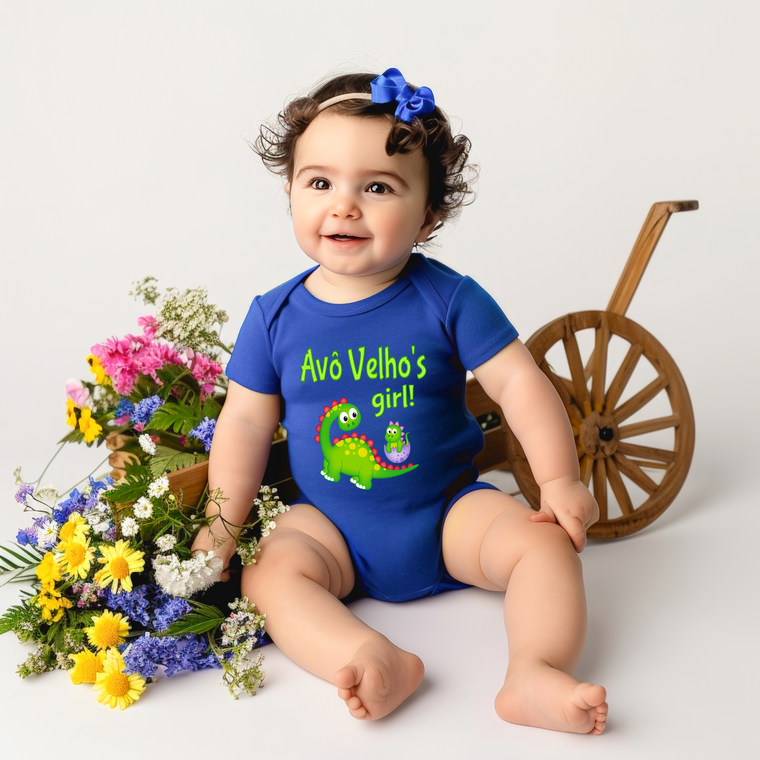 A smiling baby girl wearing a blue onesie with a dinosaur on it, sitting next to a wooden wagon and a basket of colorful flowers.