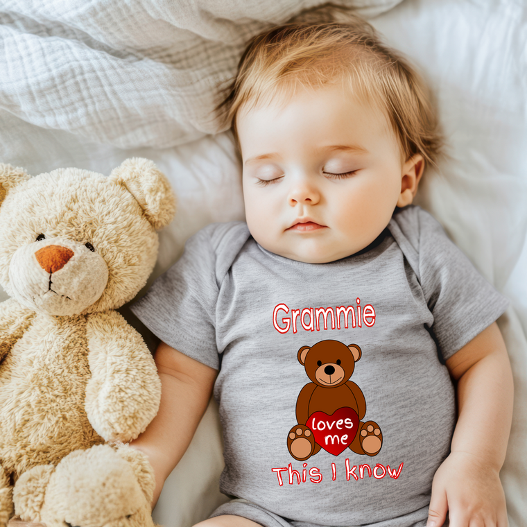 A sleeping baby wearing a gray t-shirt with a teddy bear and the text "Grammie loves me this I know" printed on it.