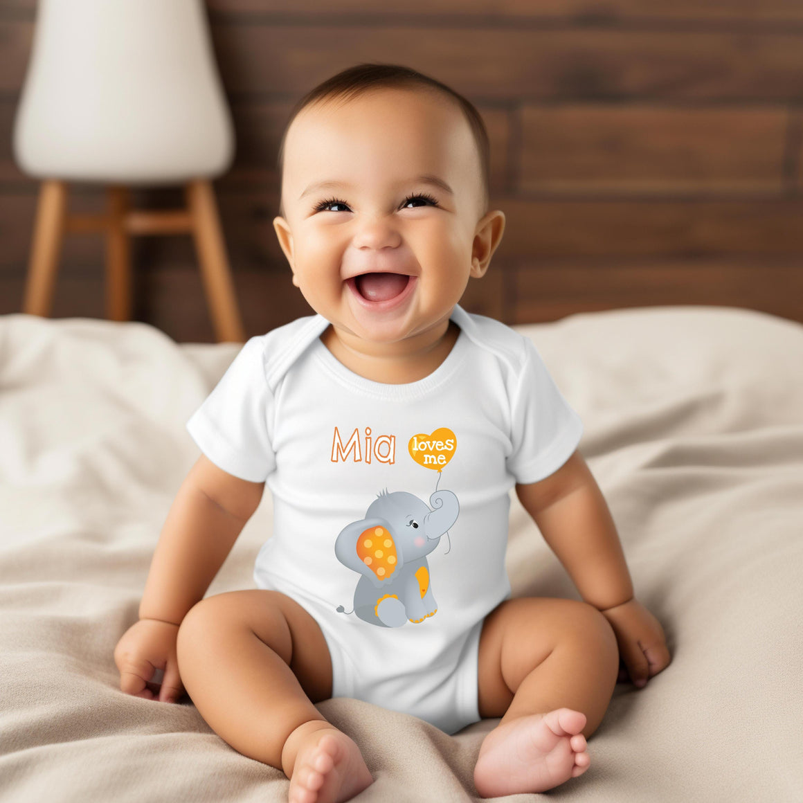 A smiling baby boy wearing a white onesie with an elephant design and the name "Mia" printed on it.
