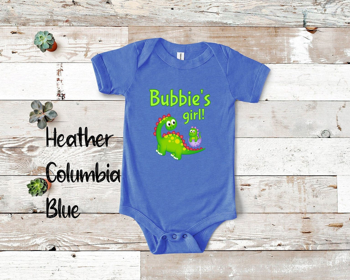 A blue baby onesie with a cartoon dinosaur and text, placed on a wooden surface.
