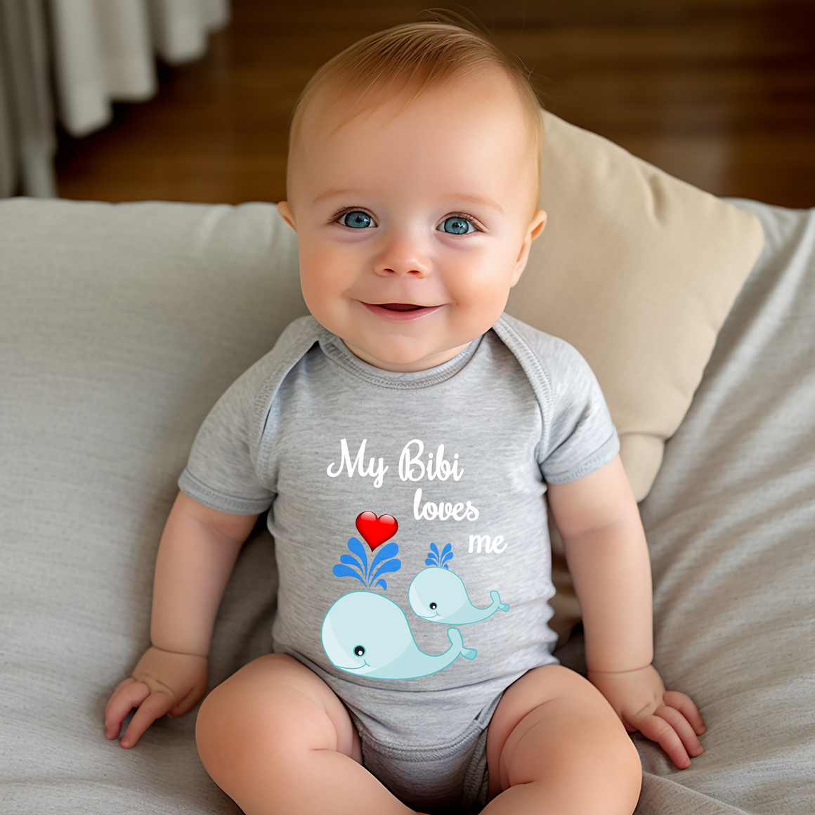 A smiling baby wearing a gray onesie with a whale design and the text "My Bibi loves me" is sitting on a couch.
