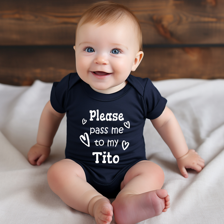A smiling baby wearing a navy blue onesie with the text "Please pass me to my Tito" printed on it.