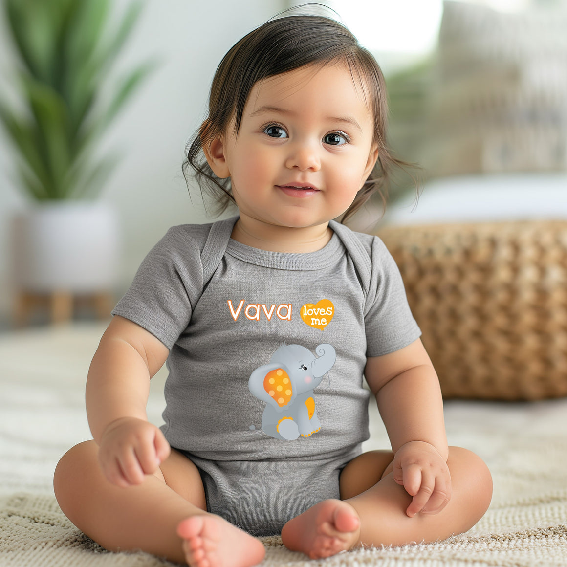 A smiling baby girl wearing a grey onesie with an elephant design sits on a beige rug.