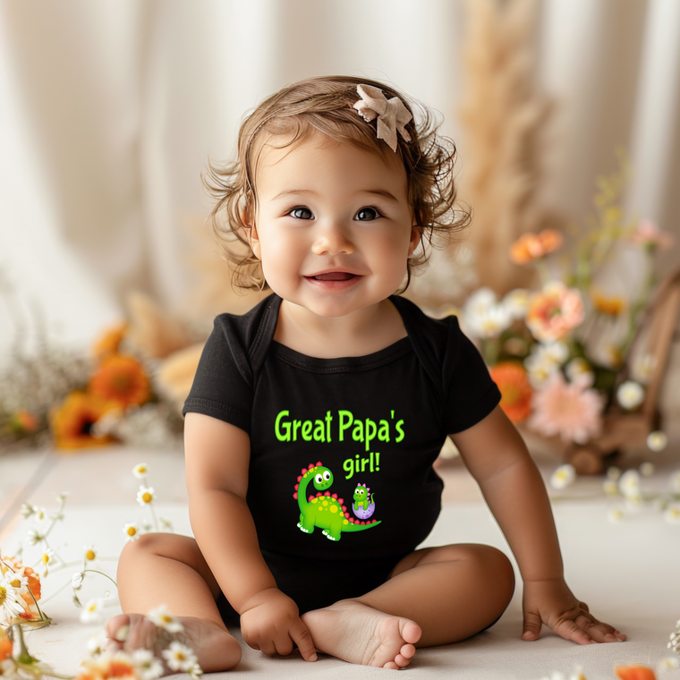 A smiling baby girl wearing a black shirt with a dinosaur and the text "Great Papa's girl!" in green.