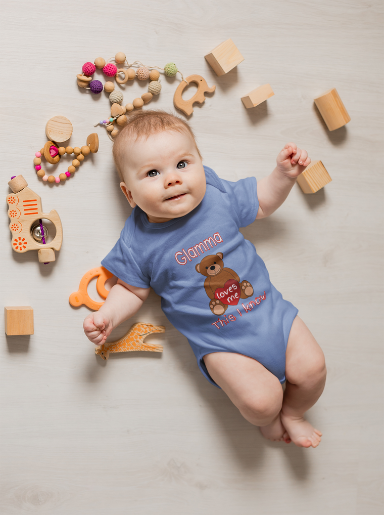 A baby lies on a white floor surrounded by various toys, including wooden blocks, a teddy bear, and a giraffe.