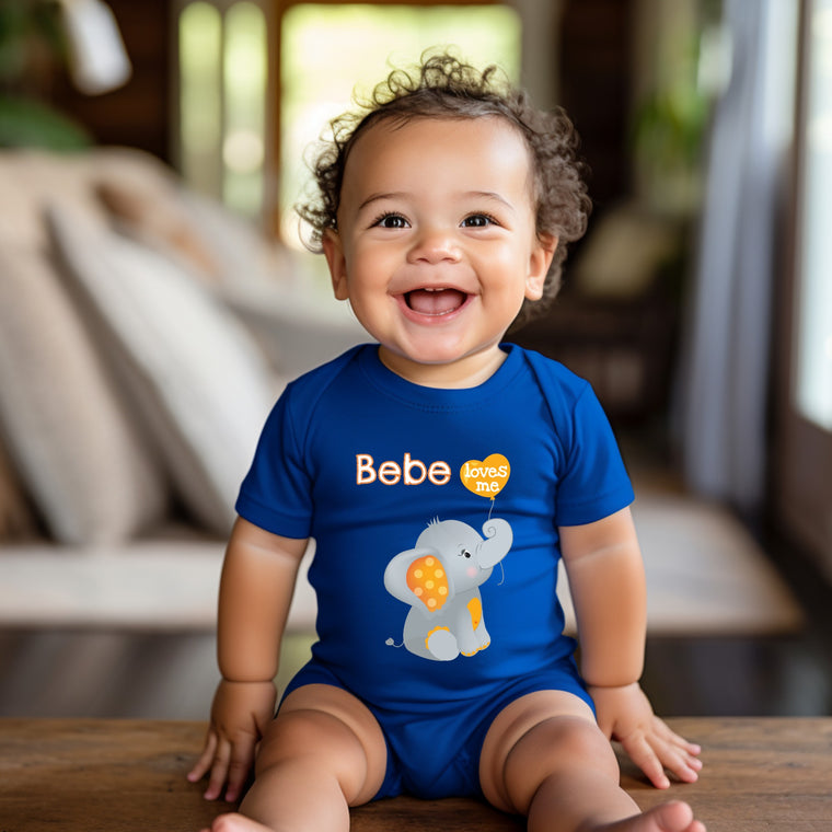 A smiling baby boy wearing a blue onesie with an elephant design sits on a wooden surface.