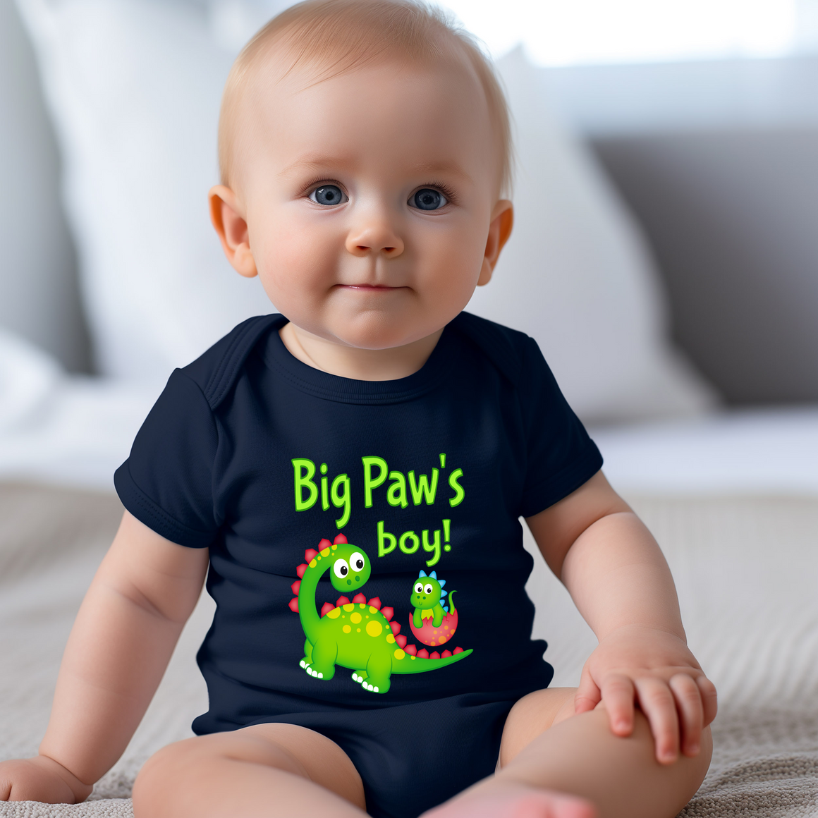 A smiling baby wearing a black t-shirt with a dinosaur graphic and text that says "Big Paw's boy!"