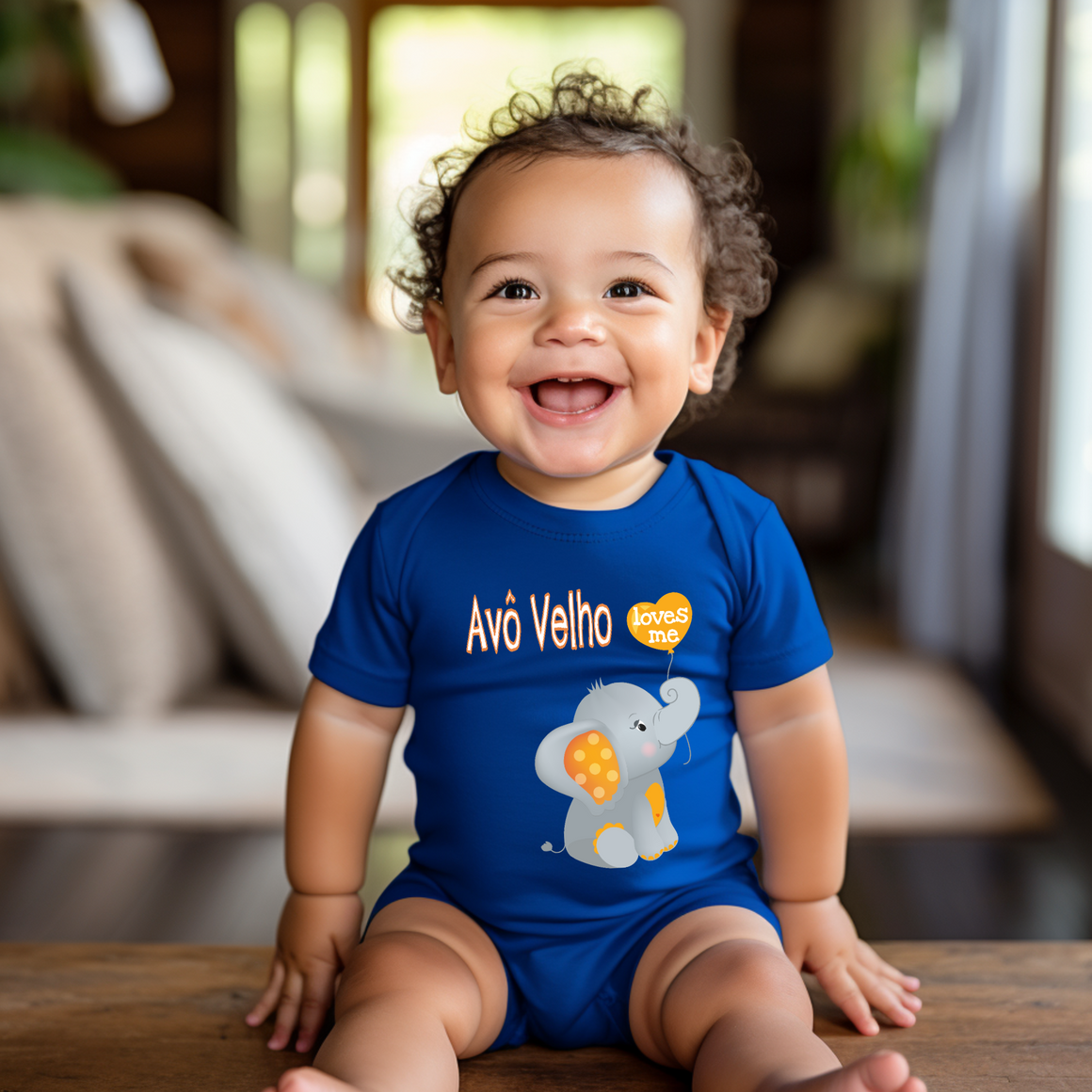 A smiling baby boy wearing a blue onesie with an elephant design sits on a wooden surface.
