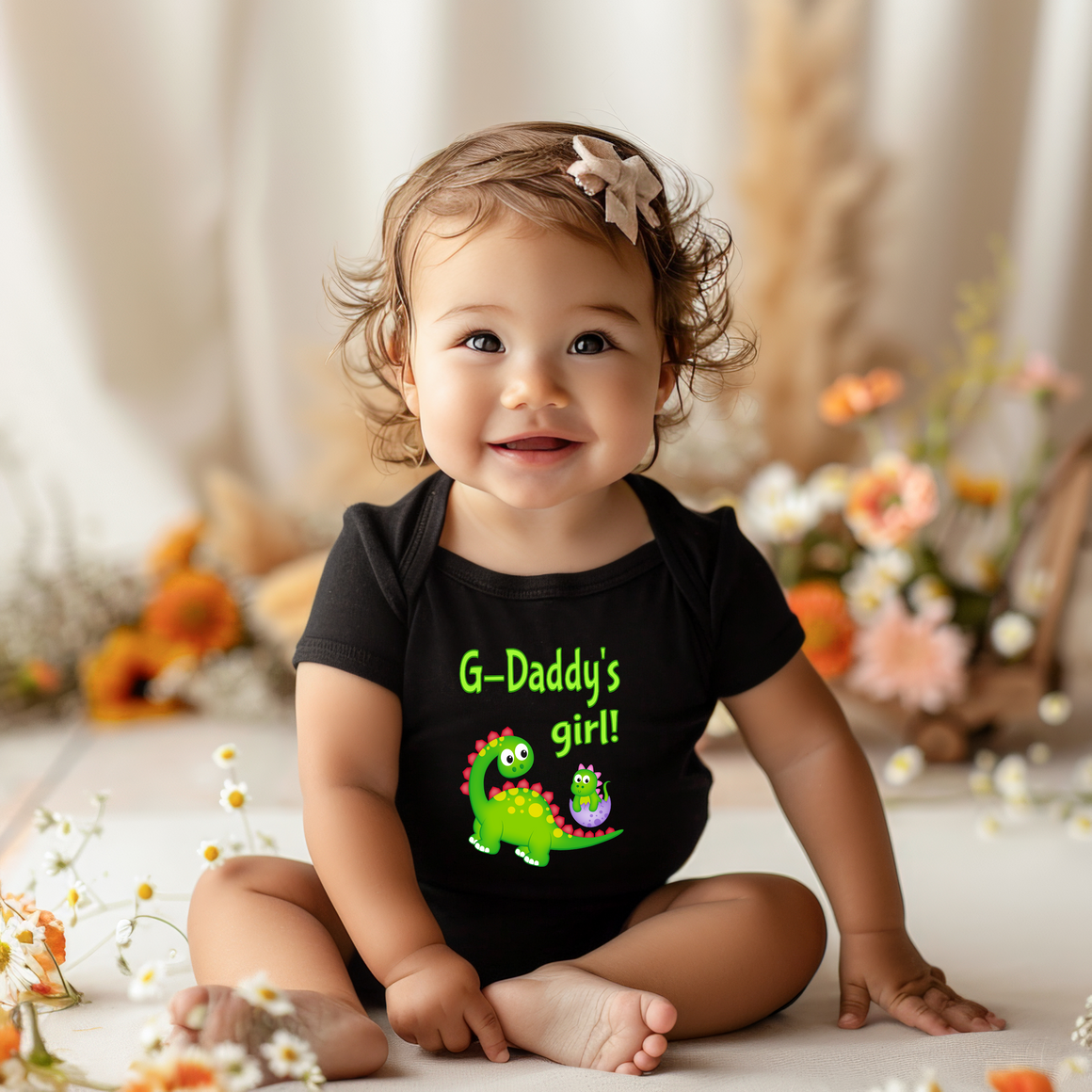 A smiling baby girl wearing a black t-shirt with a dinosaur graphic and the text "G-Daddy's girl!"