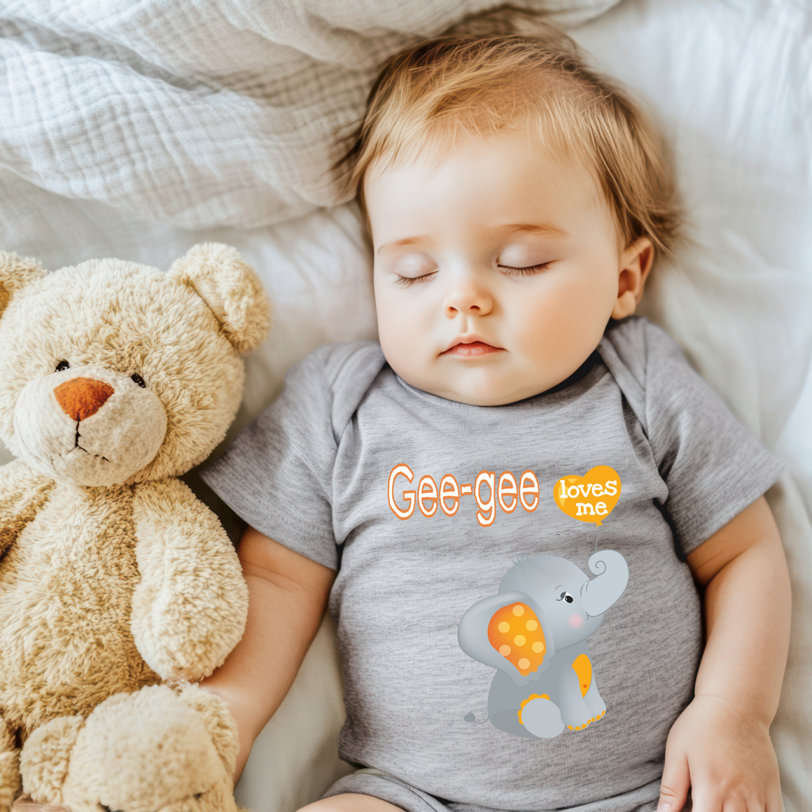 A sleeping baby wearing a gray onesie with an elephant design and the text "Gee-gee loves me" is lying next to a brown teddy bear.
