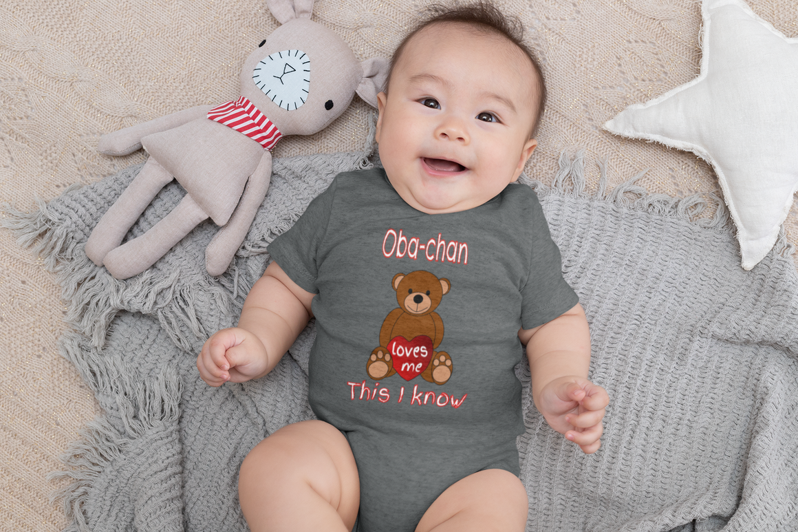 A baby wearing a gray onesie with a teddy bear and text on it, lying on a gray blanket.