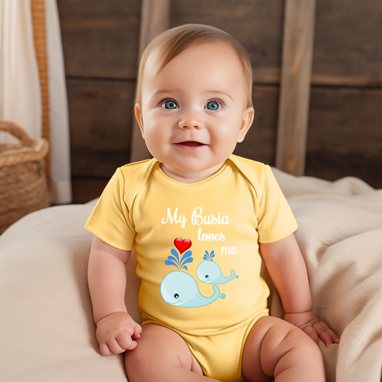 A smiling baby wearing a yellow onesie with a whale design and the text "My Busia loves me" printed on it.