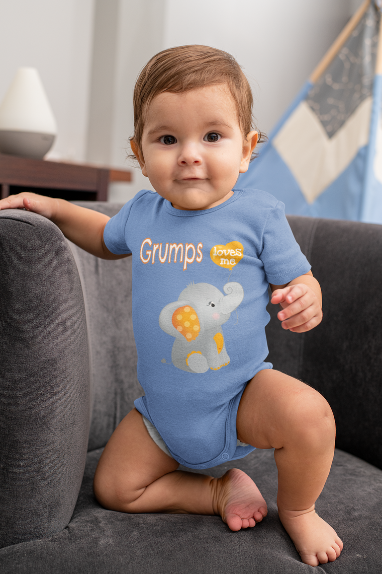 A smiling baby boy wearing a blue onesie with an elephant design, sitting on a couch.