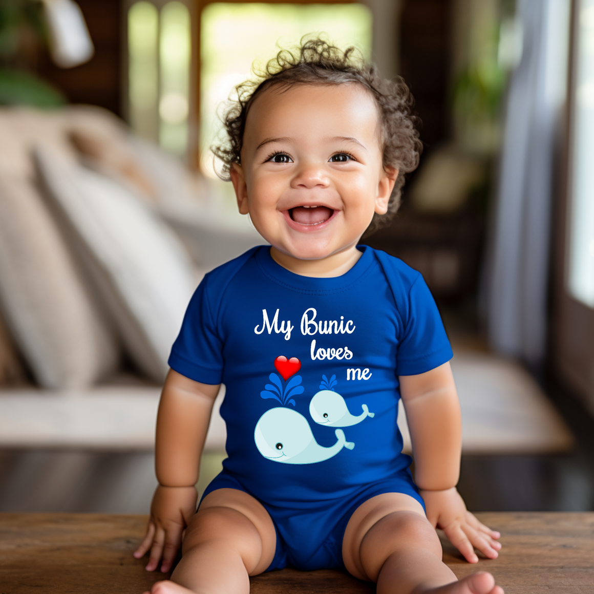A smiling baby boy wearing a blue onesie with a whale design and the text "My Bunic loves me" is sitting on a wooden surface.
