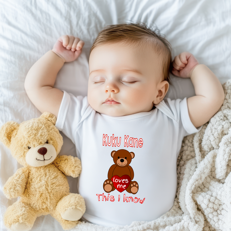 A sleeping baby wearing a white onesie with a teddy bear next to them.