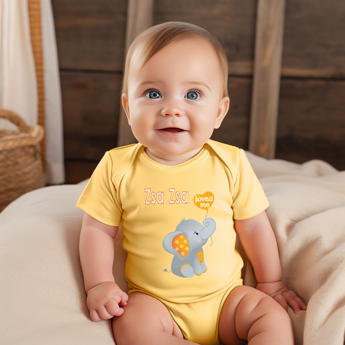 A smiling baby wearing a yellow onesie with an elephant design sits on a bed.