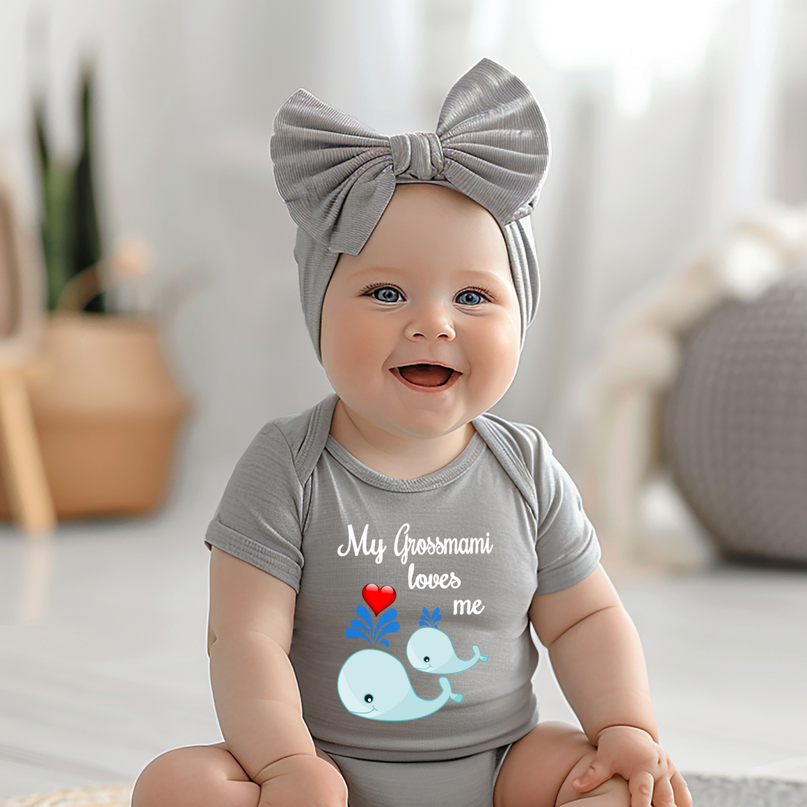 A smiling baby girl wearing a gray headband and a gray t-shirt with a graphic of a whale and the text "My Grossmami loves me".