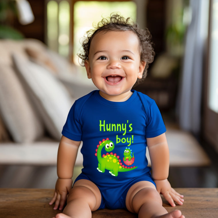 A smiling baby boy wearing a blue onesie with a dinosaur design and the text "Hunny's boy!"