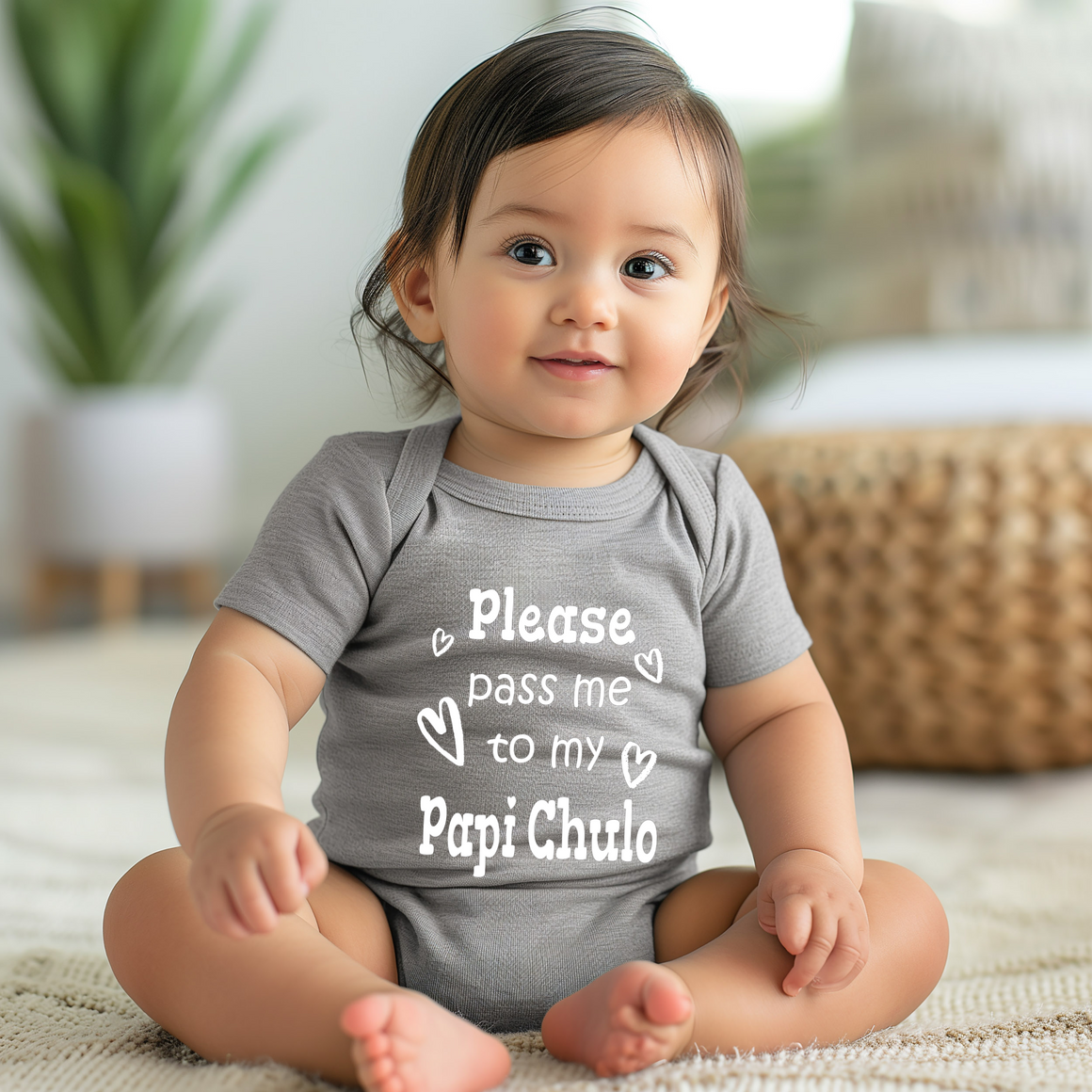 A smiling baby girl wearing a grey onesie with the text "Please pass me to my Papi Chulo" printed on it.
