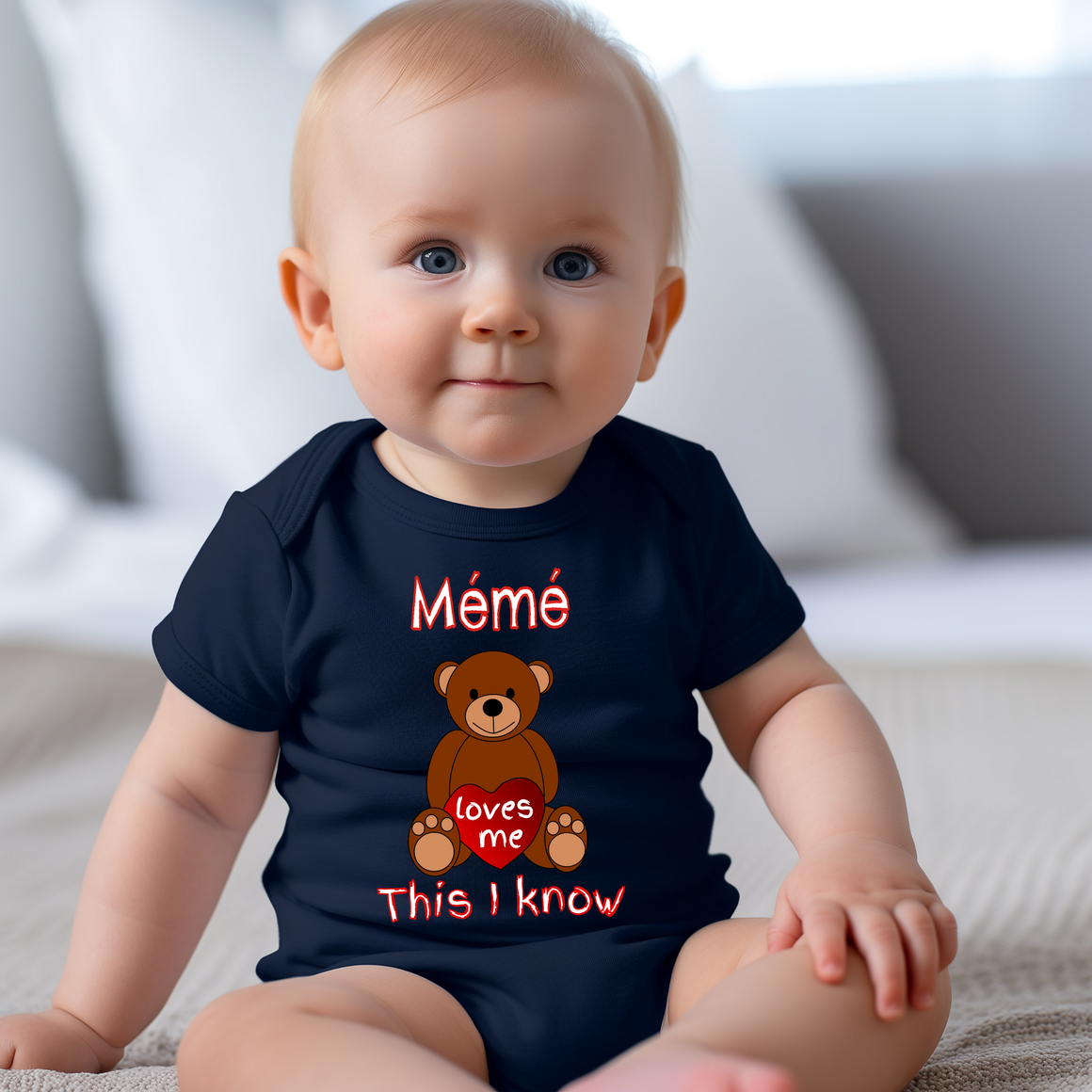 A smiling baby wearing a navy blue onesie with a teddy bear graphic and text that says "Mélè" and "loves me".